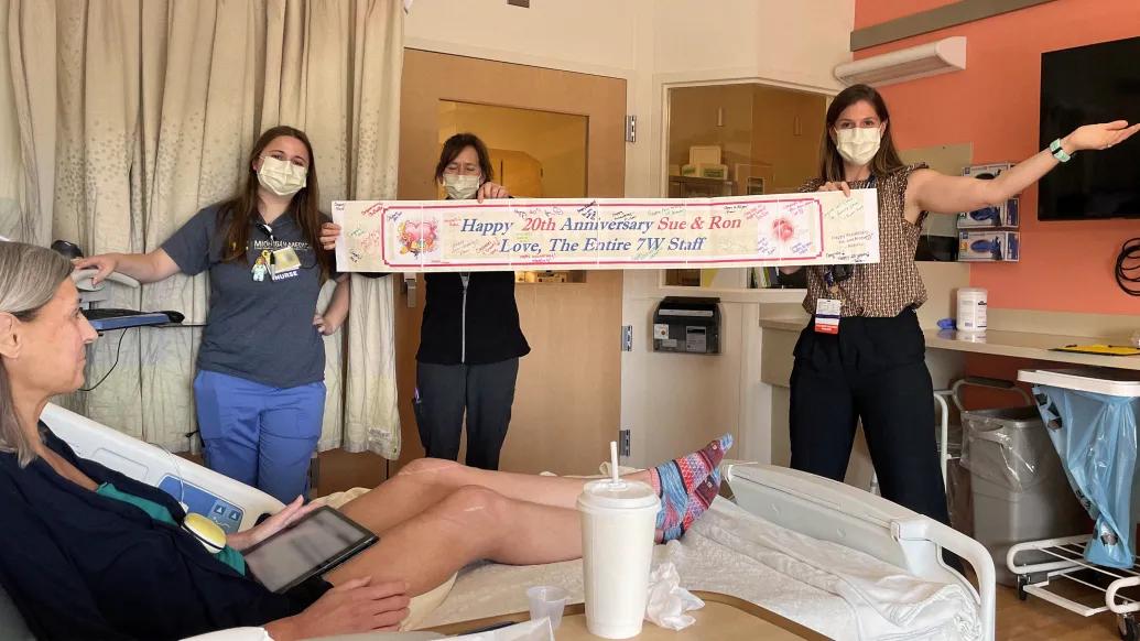 3 staff members holding up happy 20th wedding anniversary sign to patient in bed