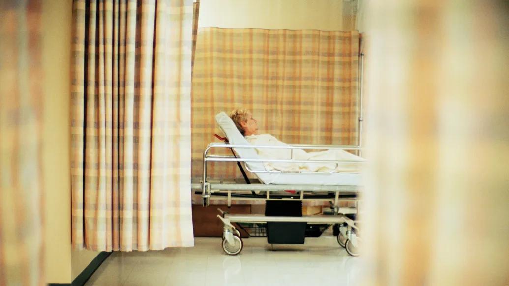 man in hospital bed through curtains that are off orange beige