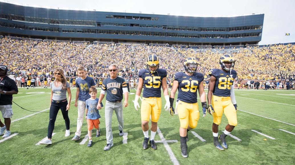 Nathan and Catherine Forbes were honorary captains during a 2015 Michigan Football game and are pictured on the field at Michigan Stadium with several players.