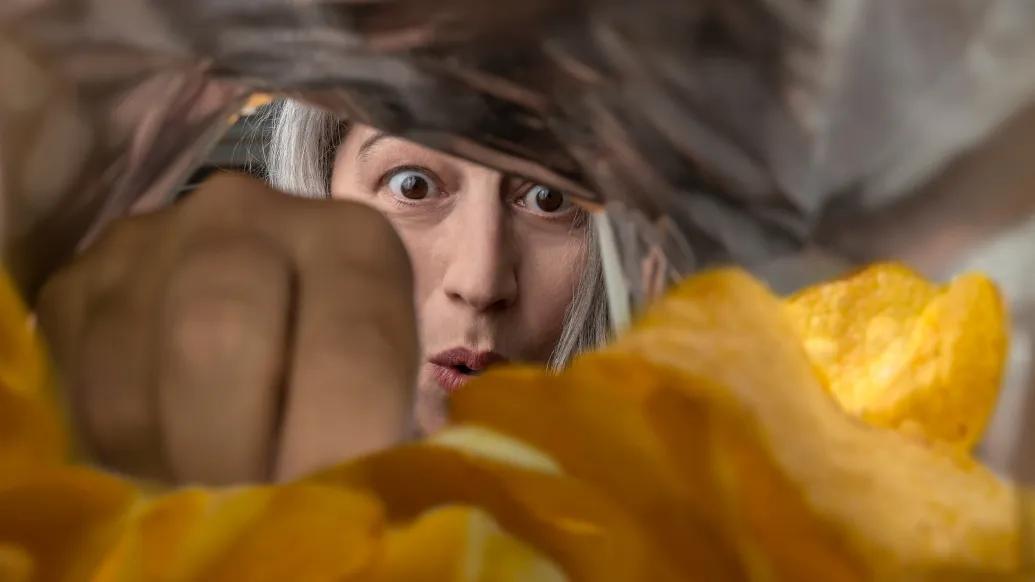 women looking into a chip bag excited you only see her face and hand going into the chips