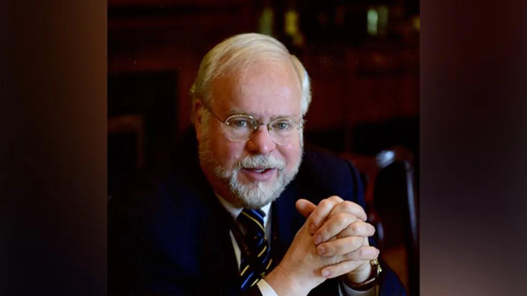 Portrait of Tim Johnson, M.D. His hands are folded in front of him, and he is wearing glasses and a dark suit and tie.