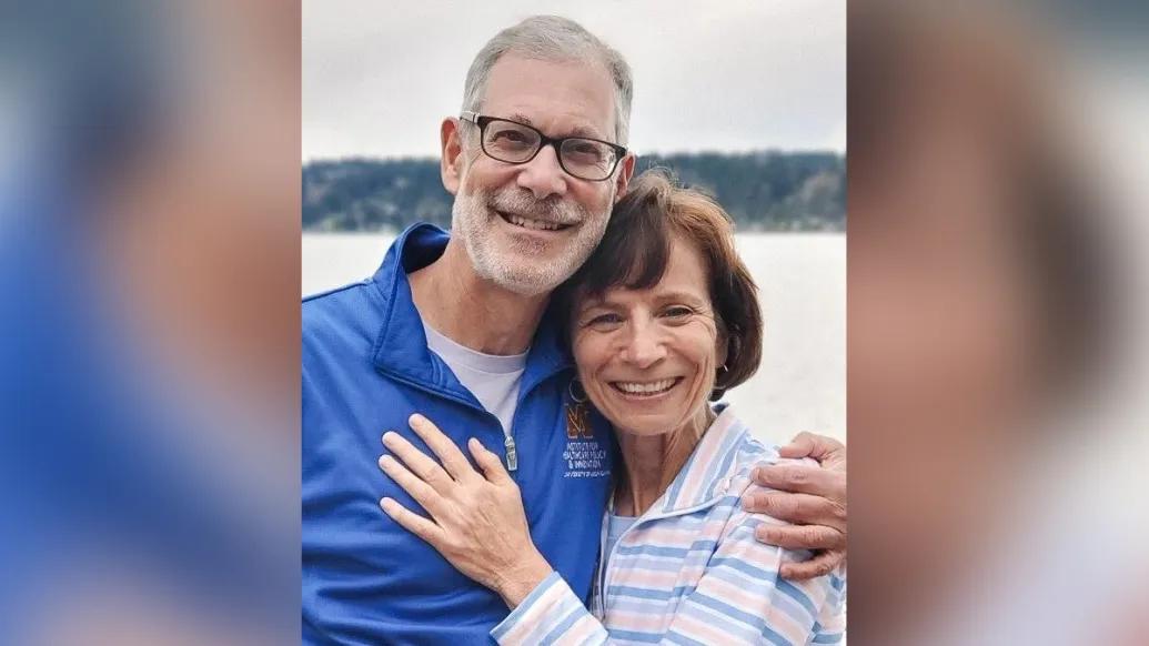 Portrait of Sandy and Hassmiller standing together in front of a lake. They are smiling with their arms around each other affectionately.