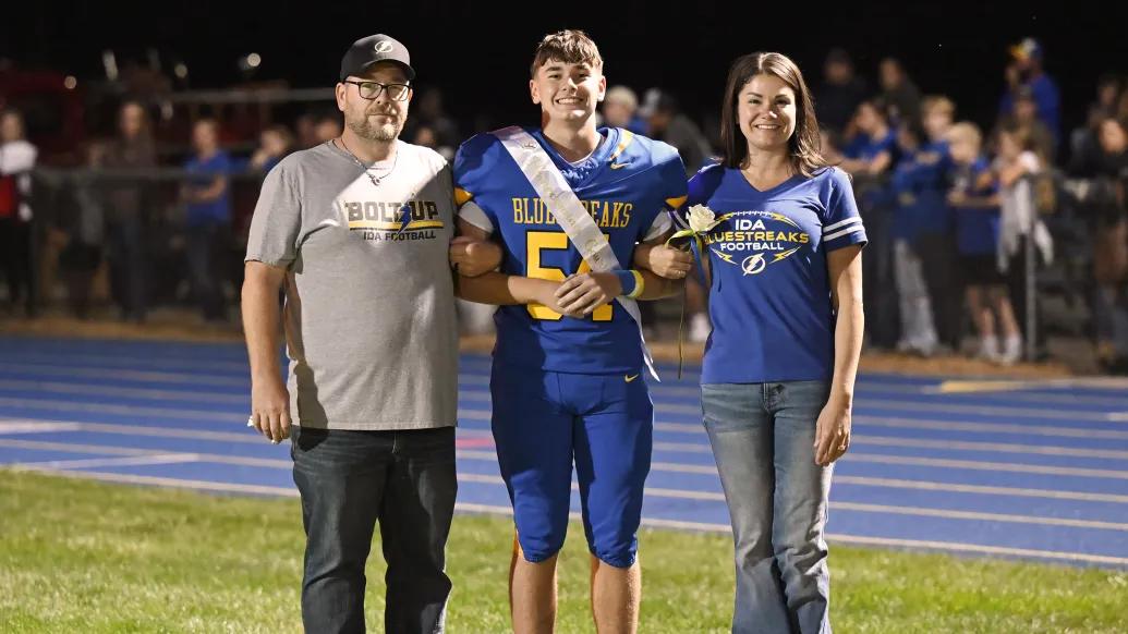 football player in middle of parents on field smiling