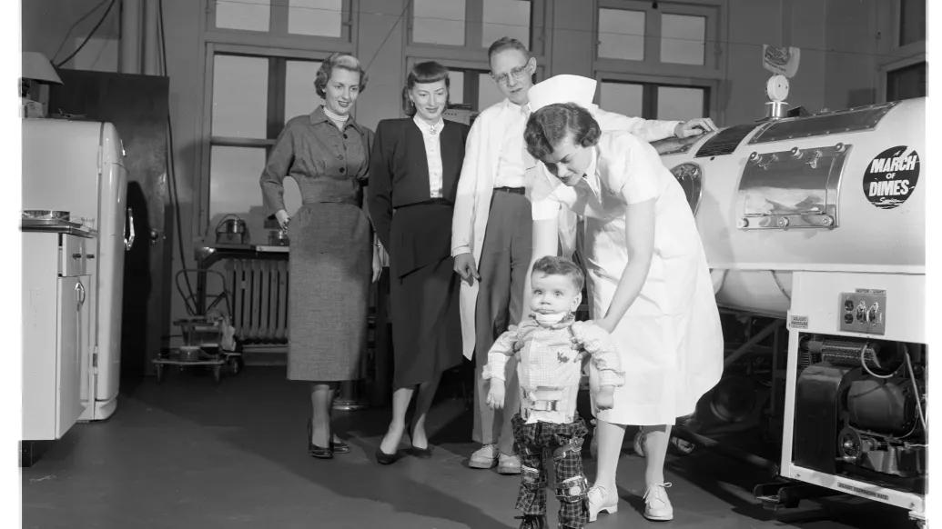 A toddler in braces near an iron lung in U-M polio unit 1950s