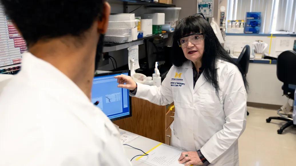 woman in white coat talking in lab with lab glasses on 