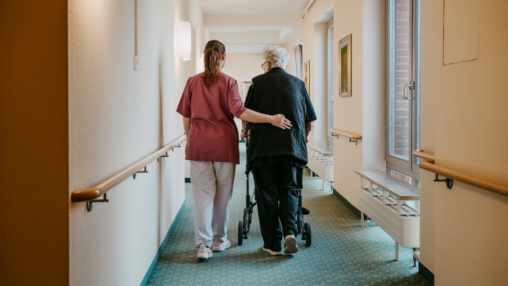 health care worker walking with older patient down hall