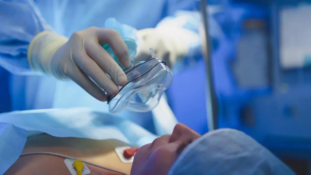 woman prepped for surgery with mask going over mouth in surgical setting blue scrubs on all pictured and white gloves 