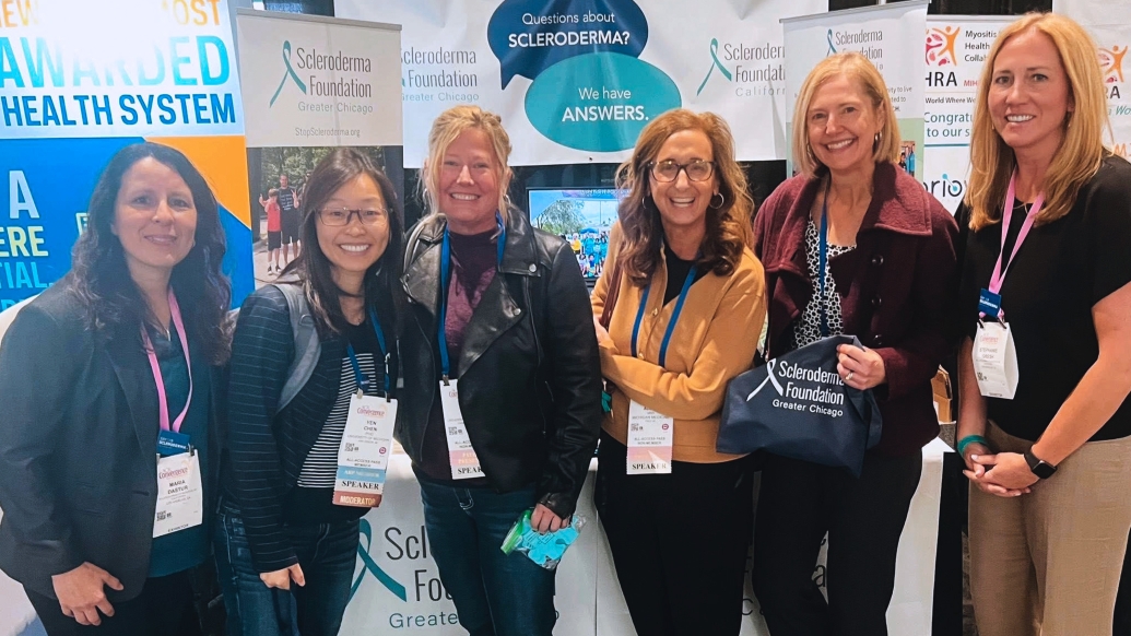 six women standing together smiling in front of posters