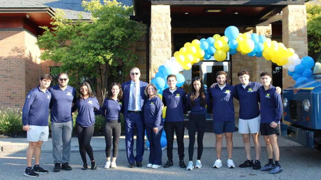 Members of the Shenandoah Young Adult Committee and others stand in front of a yellow and blue balloon arch in front of the Shenandoah Country Club.
