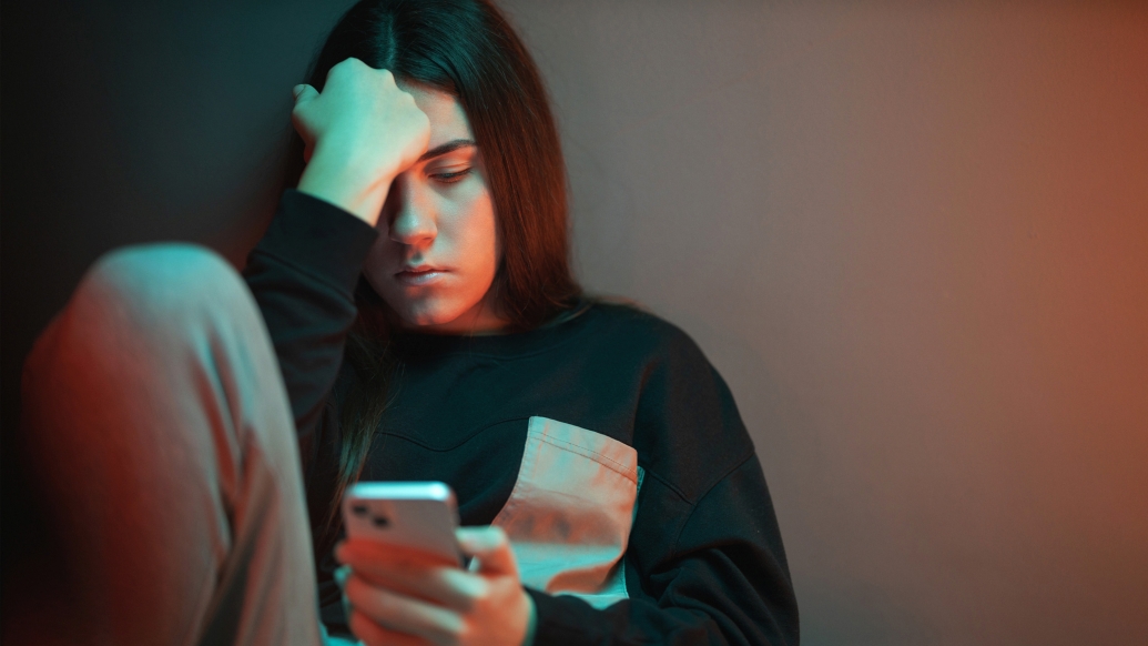 teen looking sad down at her phone dark room 