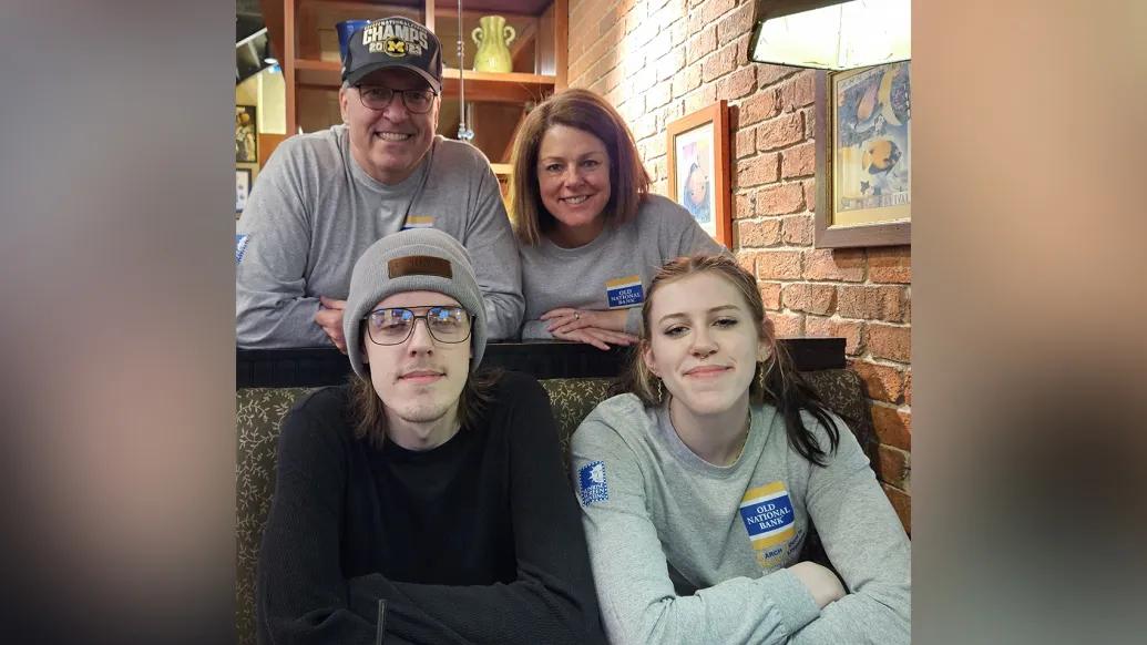 The Hepner family together in what appears to be their living room. The two young adults are seated on a couch and the two parents lean in behind them. All are smiling.