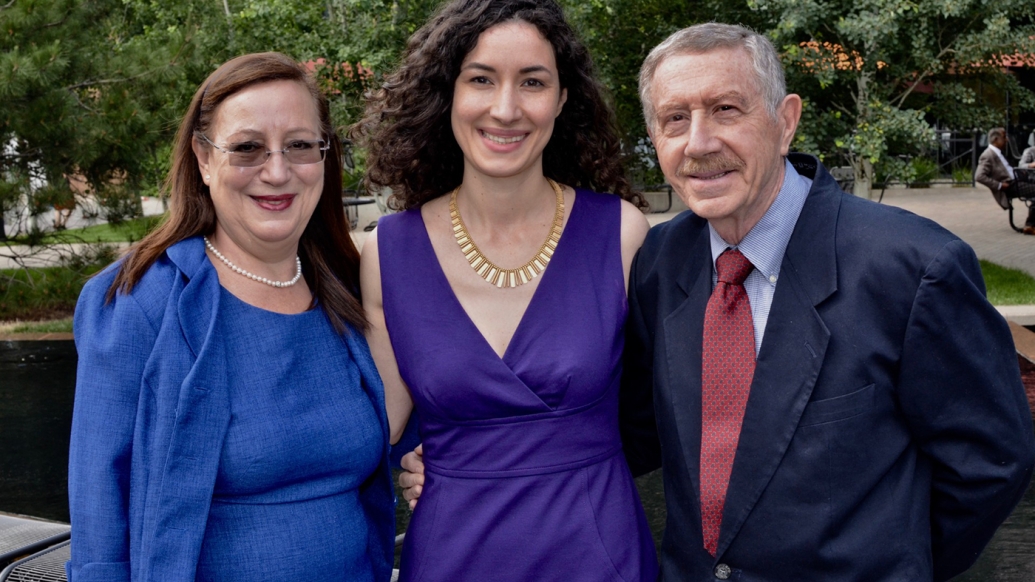From left to right, Giuseppina, Giulia, and Robert Ippolito smiling and standing together. They appear to be dressed for a special event. They are outside and there are trees and paved areas behind them.