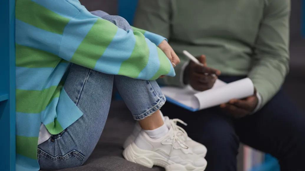 kids hugging legs with jeans on green light blue striped shirt white sneakers next to person with green shirt writing on white notepad