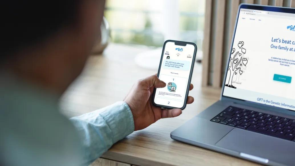man holding iphone in hand over laptop blurred