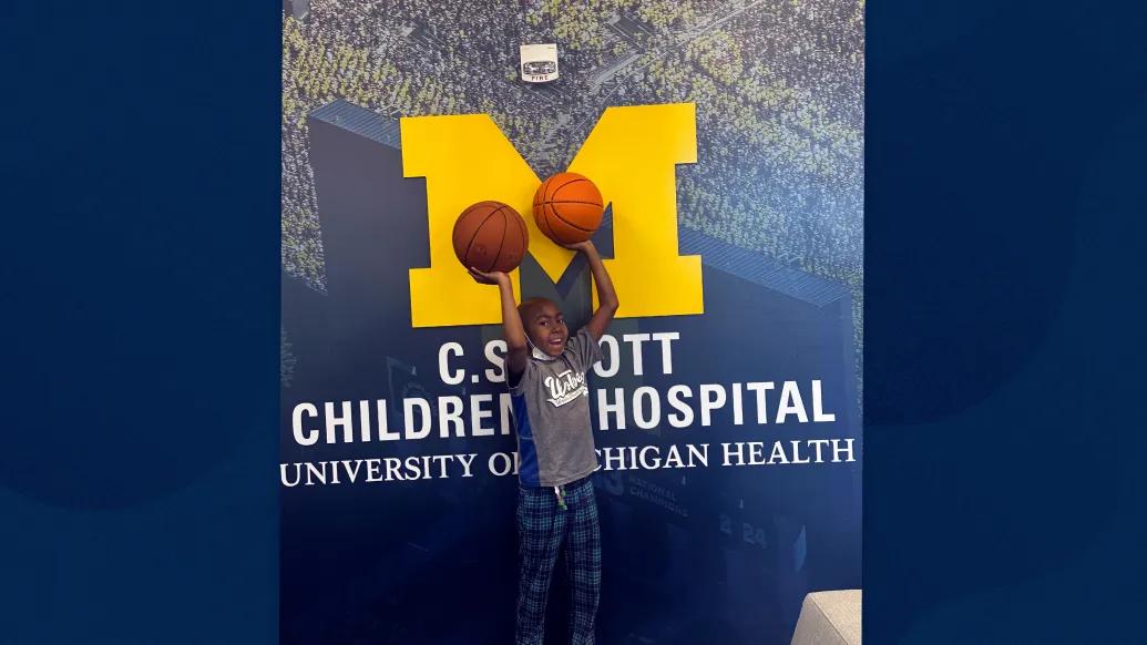 little boy with basketballs and Michigan C.S. Mott logo behind him