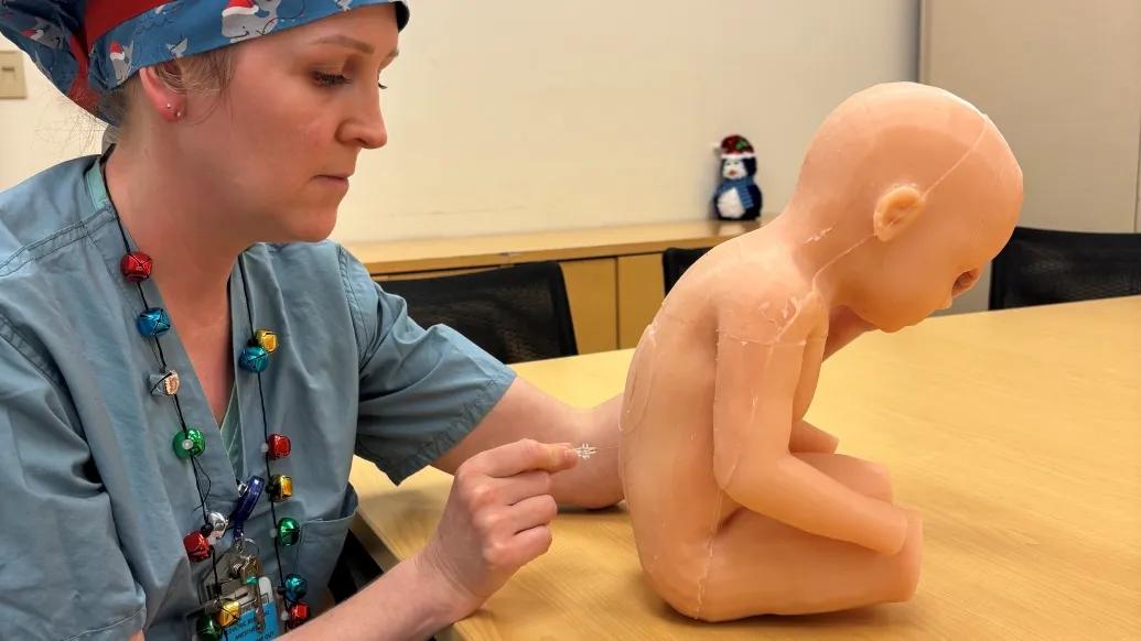 doctor in scrubs with doll baby doing spinal tap in back in conference room on table