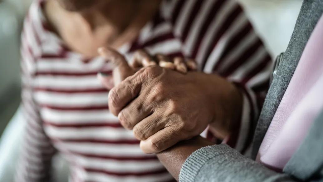 Nurse or home caregiver and senior woman holding hands at home