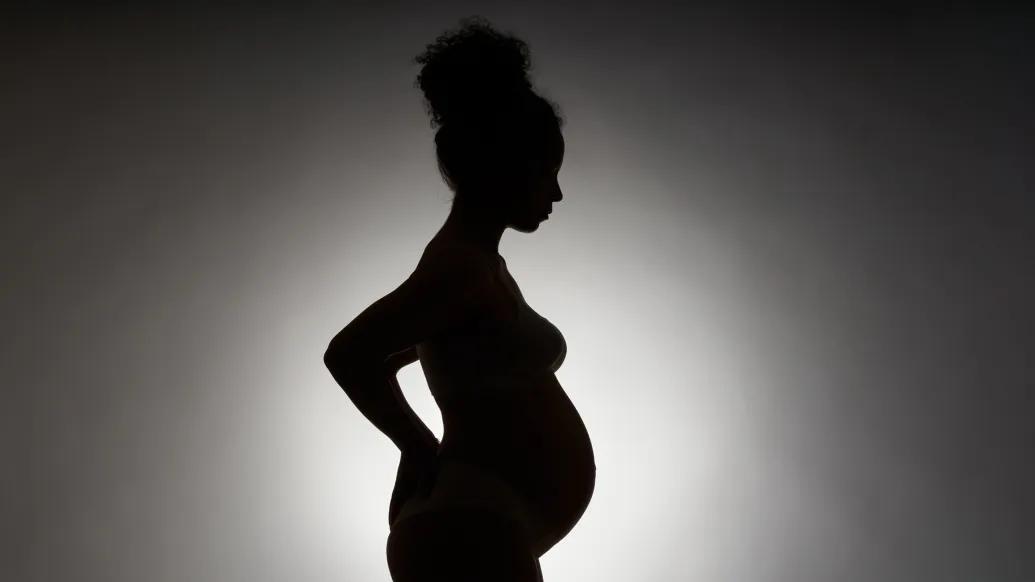 silhouette of pregnant woman black on grey background with white background behind the body glowing
