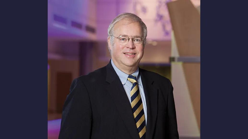 Portrait of Timothy Johnson wearing a suit and tie and standing in the lobby of a University of Michigan hospital