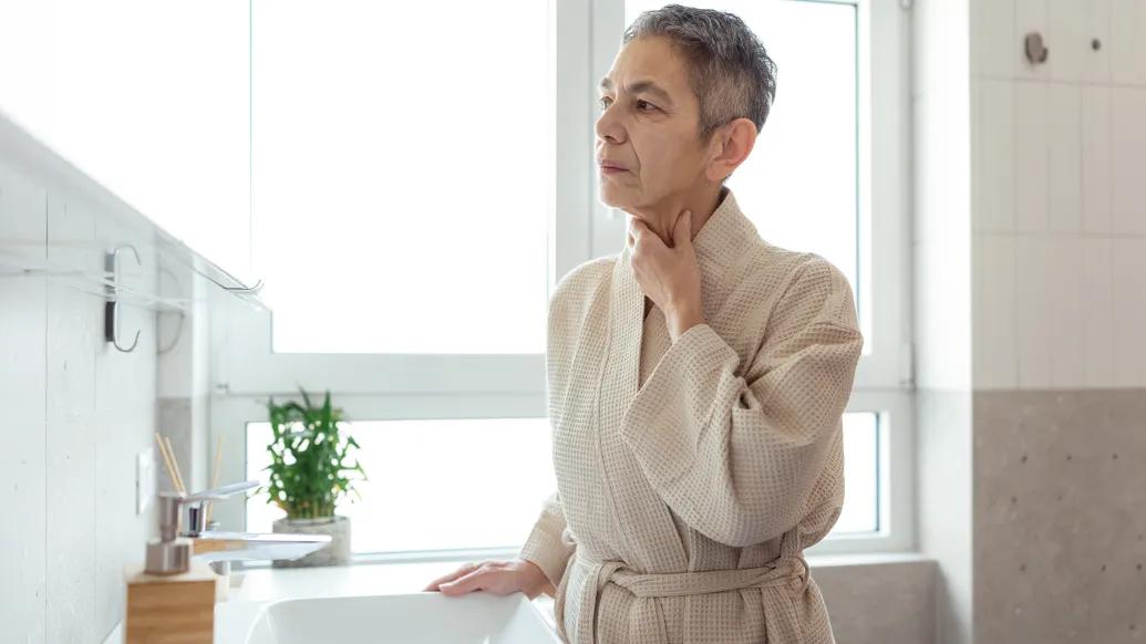 woman touching her neck in robe at home