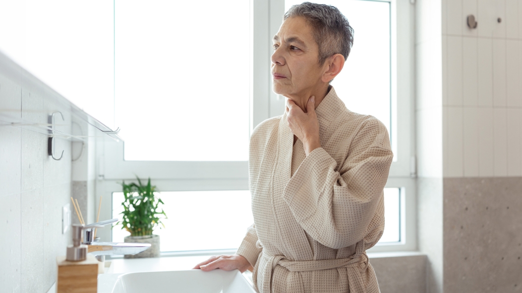 woman touching her neck in robe at home