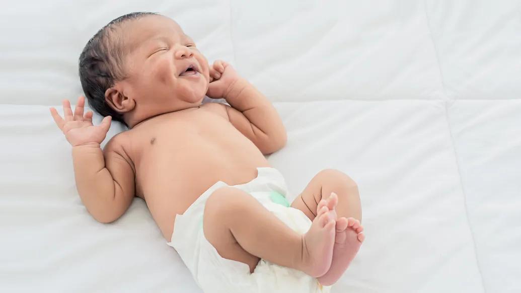 baby laughing on bed in diaper