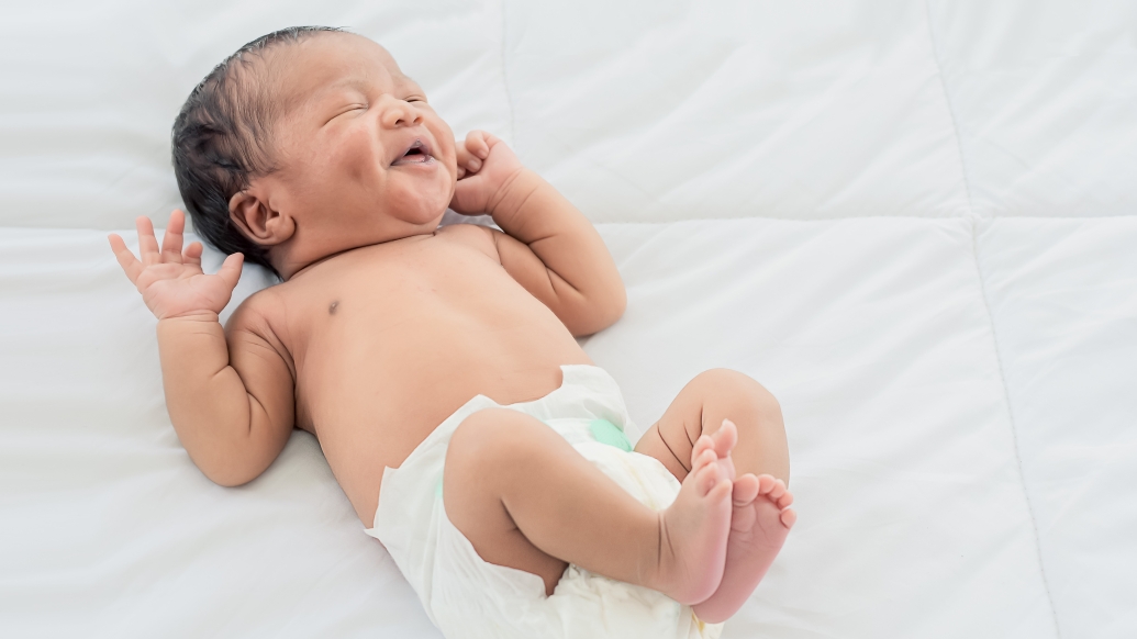 baby laughing on bed in diaper
