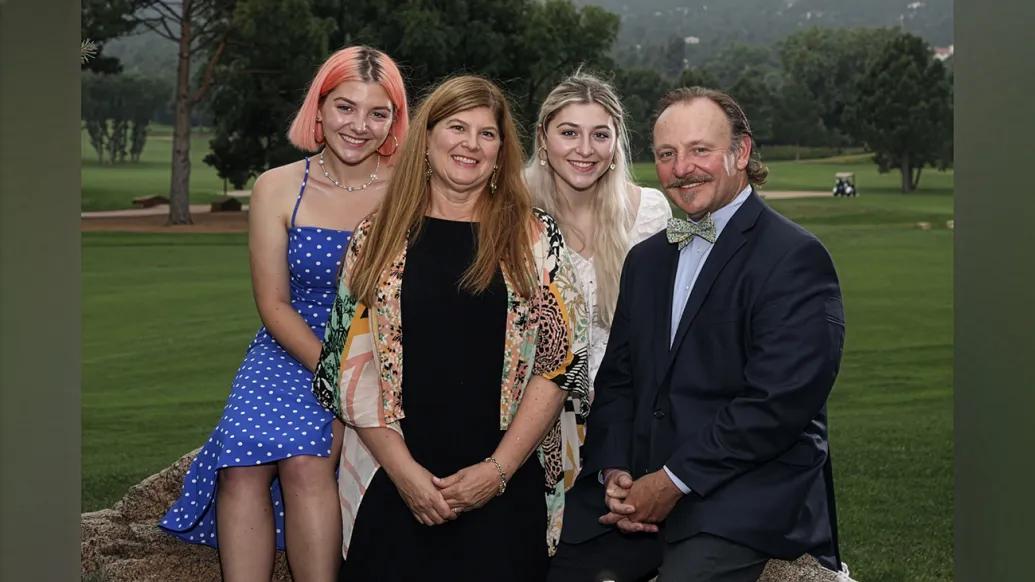The Bonnell family, including Laura, Michael, and their two daughters, Emily and Molly, seated together with a golf course in the background.