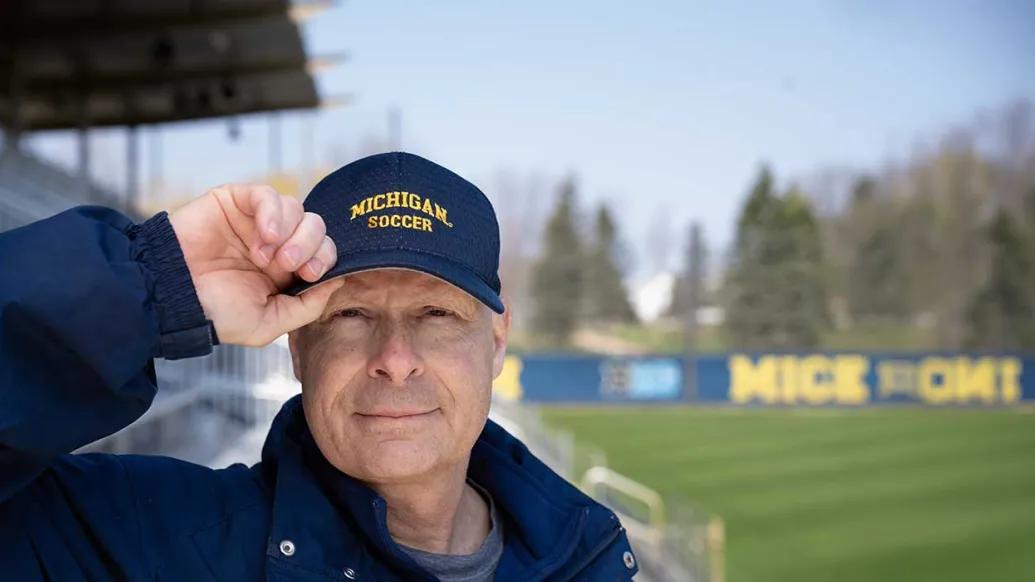 Steve Burns wearing his University of Michigan soccer hat while standing on the Michigan soccer field