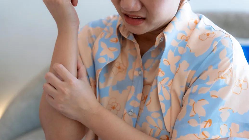 woman itching skin orange blue button down