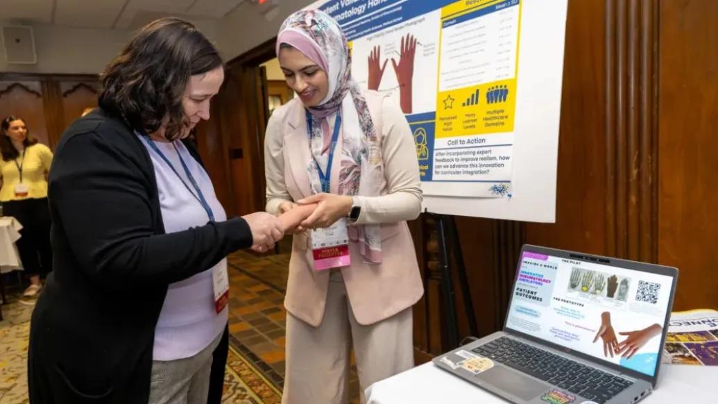 women looking at model hand in front of poster and computer on table next to them