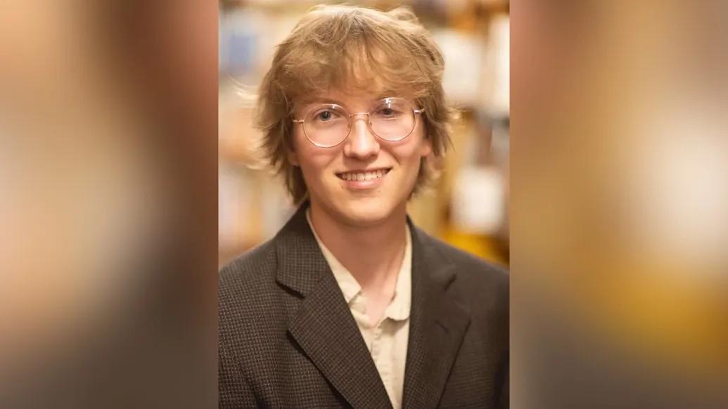 Portrait of Chase as a young adult. He is wearing glasses and a dark brown jacket over a button-down shirt.