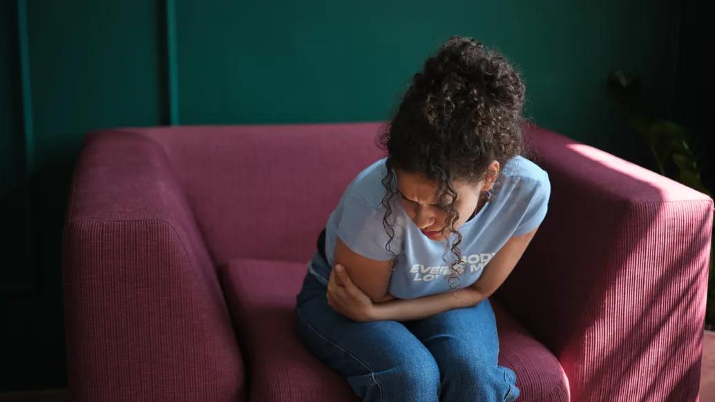getty image of a woman bending over in a red seat in pain with green painted background