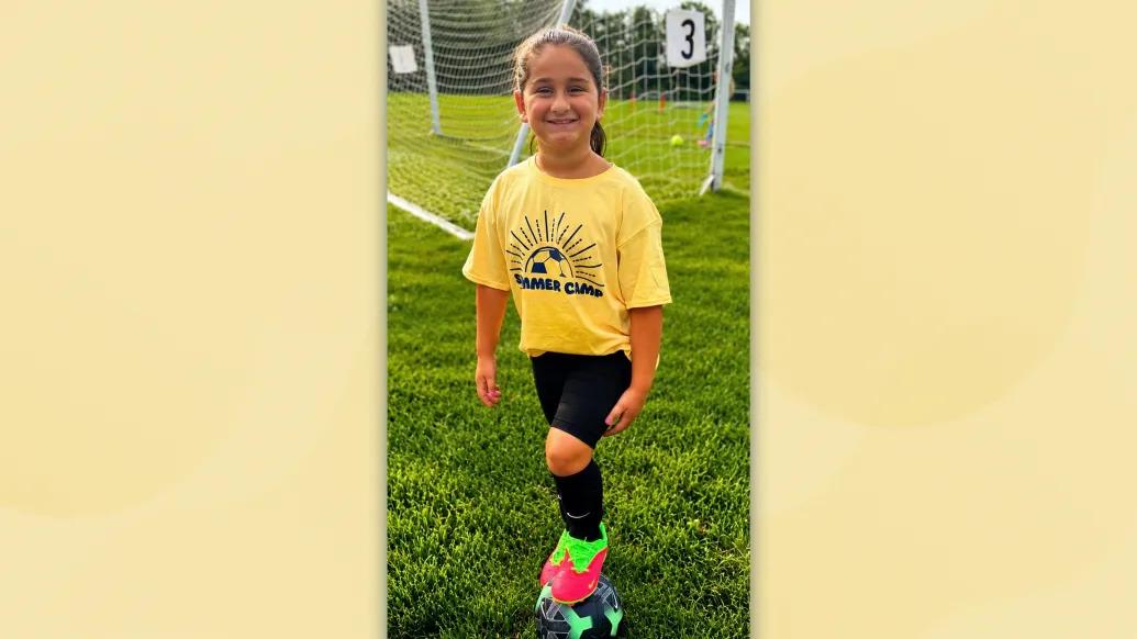 little girl with yellow shirt on soccer field smiling ready for soccer