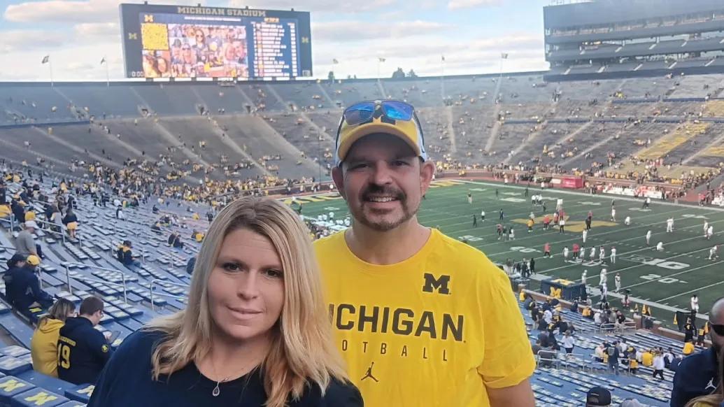 Double portrait of Jennifer Strohpaul and her fiancé standing together with the Big House visible behind them.
