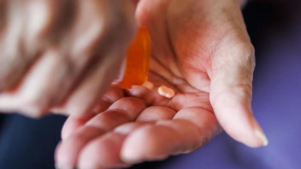 A pill bottle is open and pills are placed onto a hand