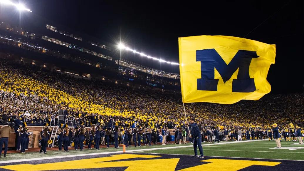 Man holding UM flag on UM football field, athletics