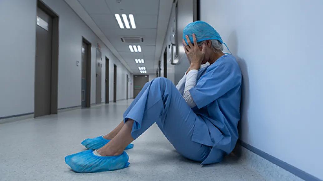 female surgeon on ground upset hands to face in scrubs and scrub shoes