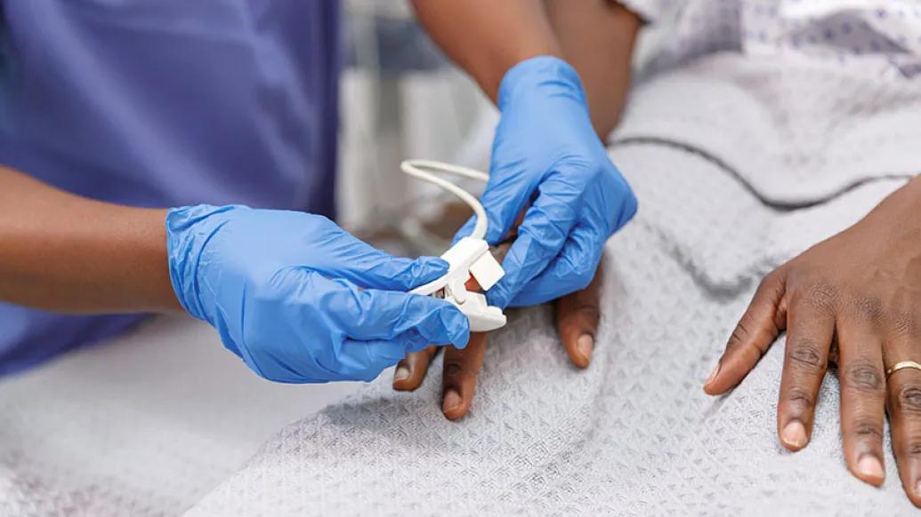 Patient in hospital bed having oxygen reading by provider with blue gloves on