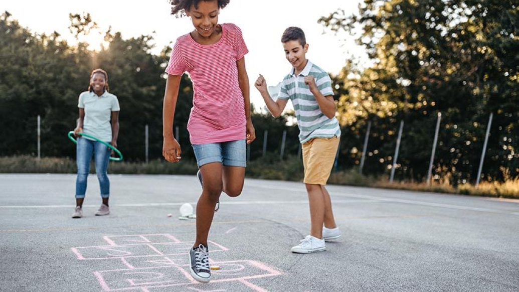 children playing hopscotch outside with no masks and trees on pavement