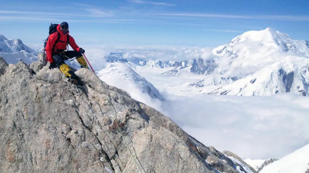 Climber in red coal sitting on mountain summit