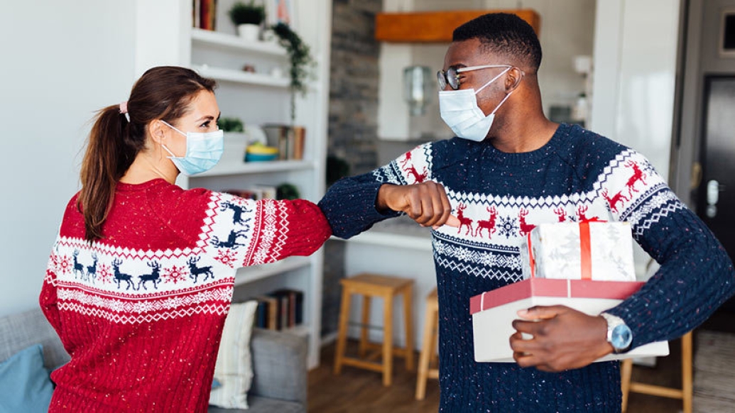 two people bumping elbows in masks in holiday sweaters red and navy