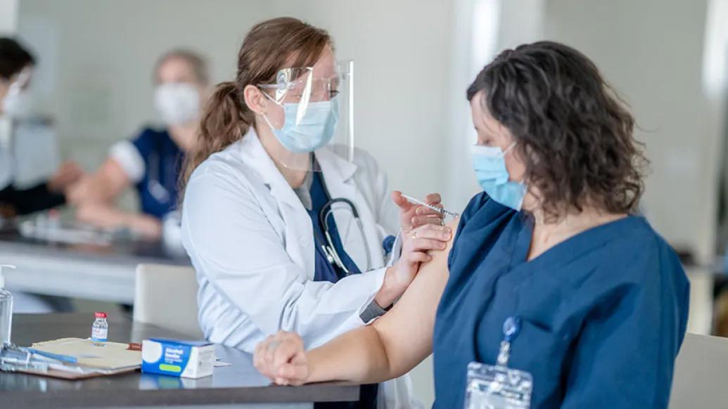 health care worker with face shield giving shot to woman with both wearing masks