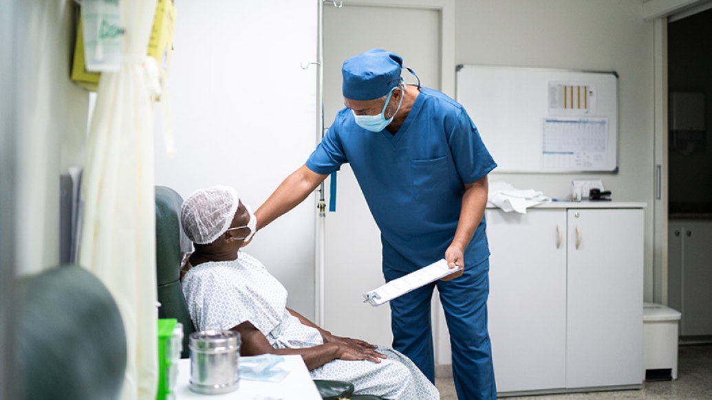 doctor in mask with clipboard reaching down to patients shoulder sitting with mask on