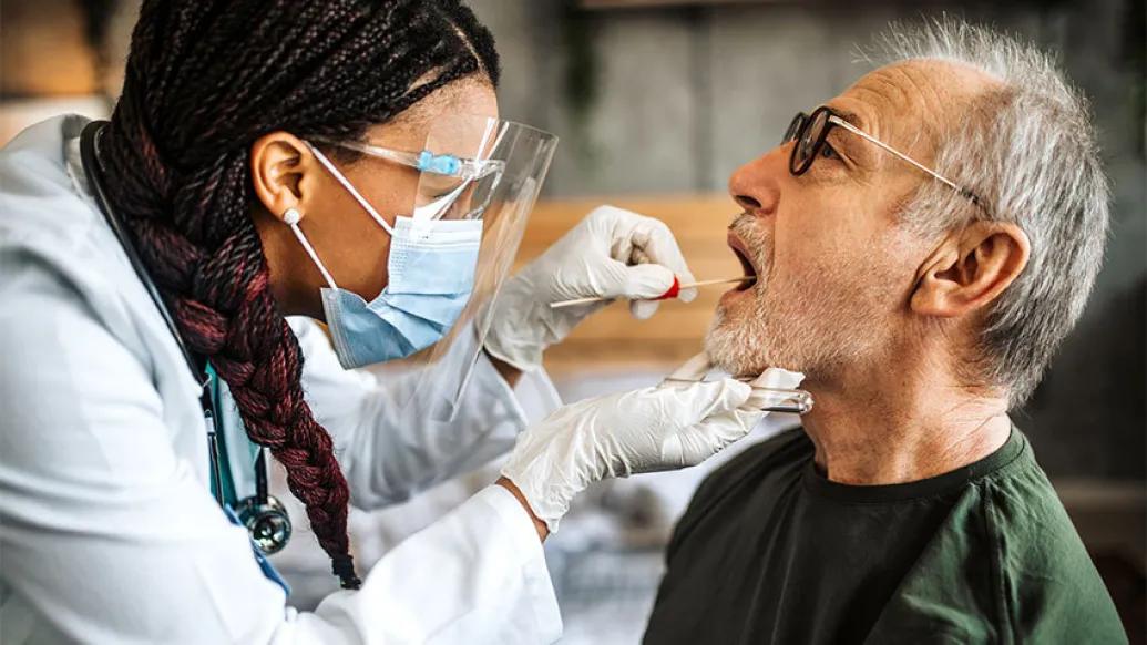 doctor swabs man's mouth with mask and eye glass gear on