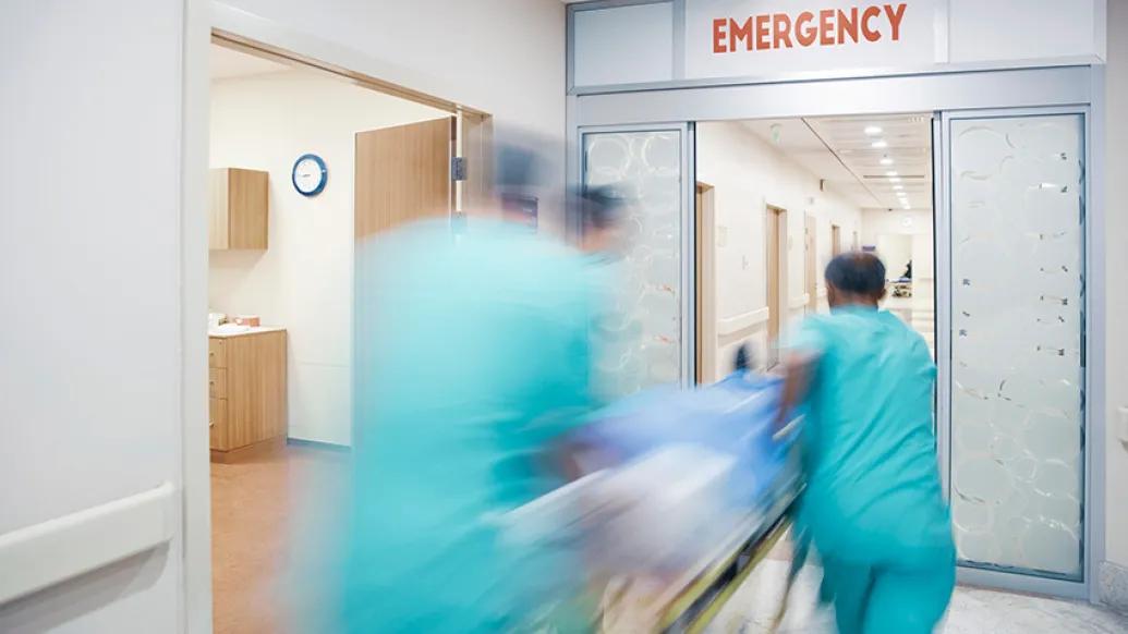 3 doctors rushing blurry into emergency room hospital in teal scrubs with stretcher