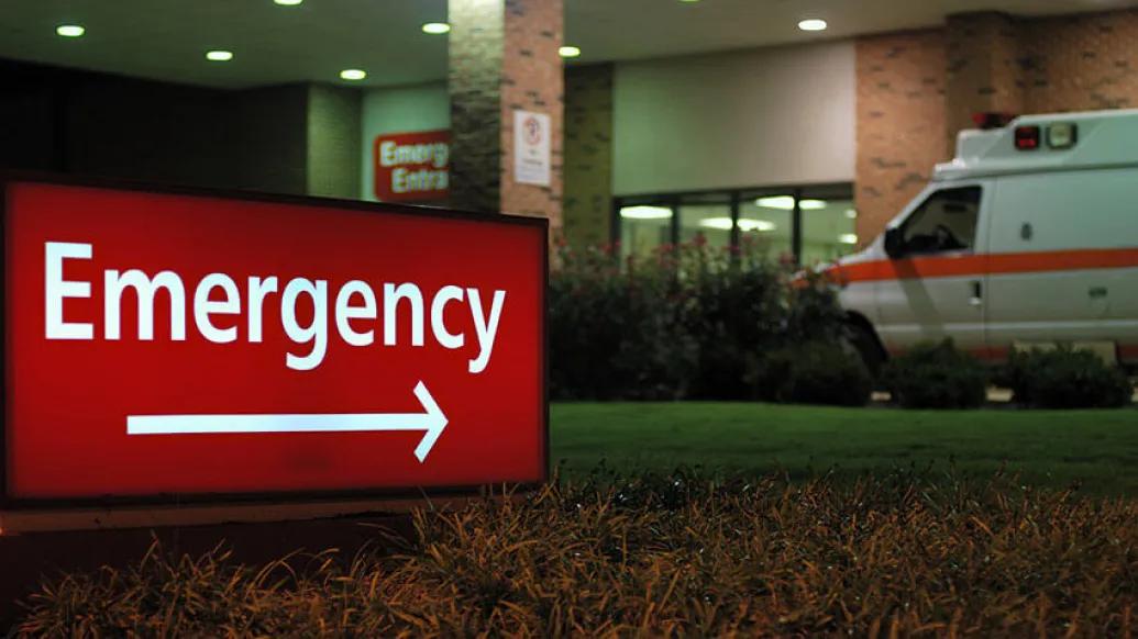 Emergency sign with hospital and ambulance in background