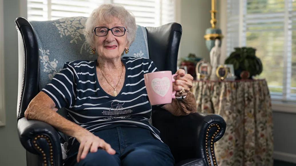 grandmother smiling with pink mug in hand in chair sitting