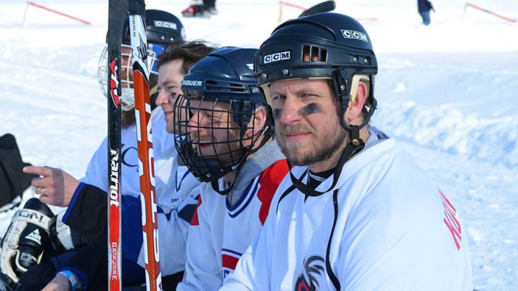 Hockey players sitting on bench with sticks snow in background