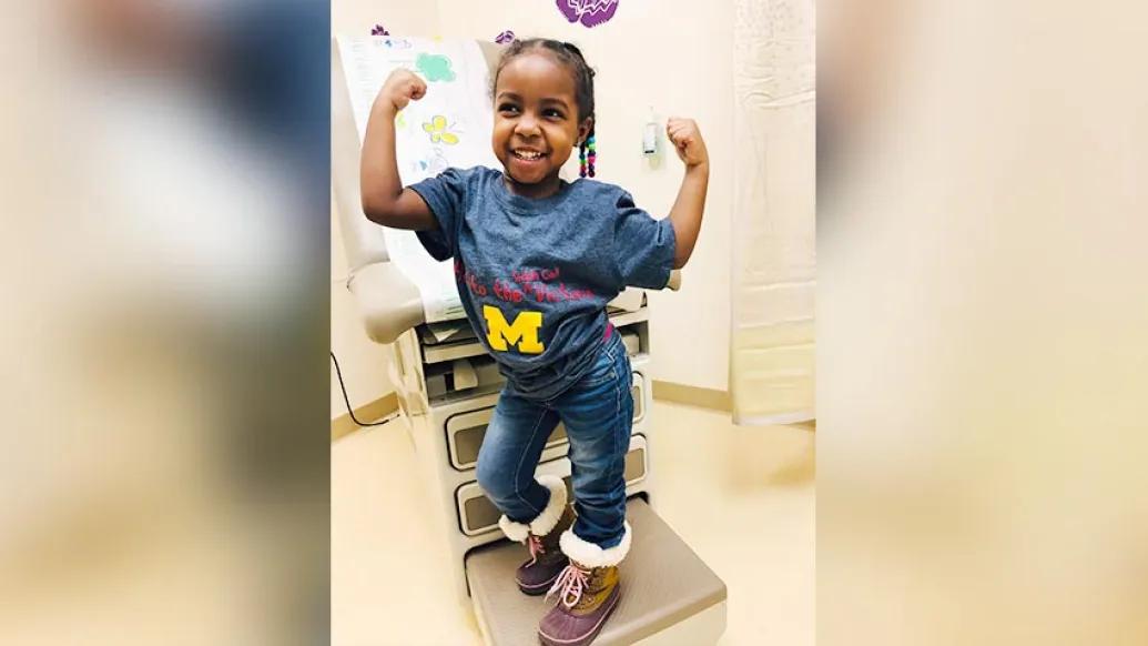 little girl doing muscle pose in doctor's office wearing a blue Michigan shirt
